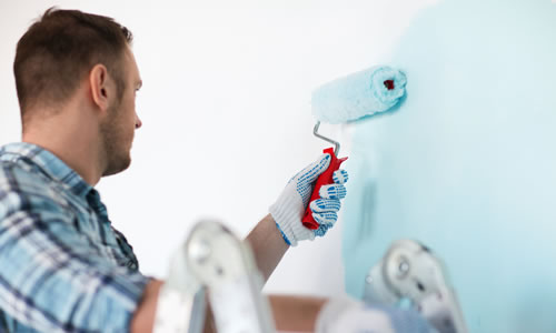 Painter using roller to paint wall with light blue paint